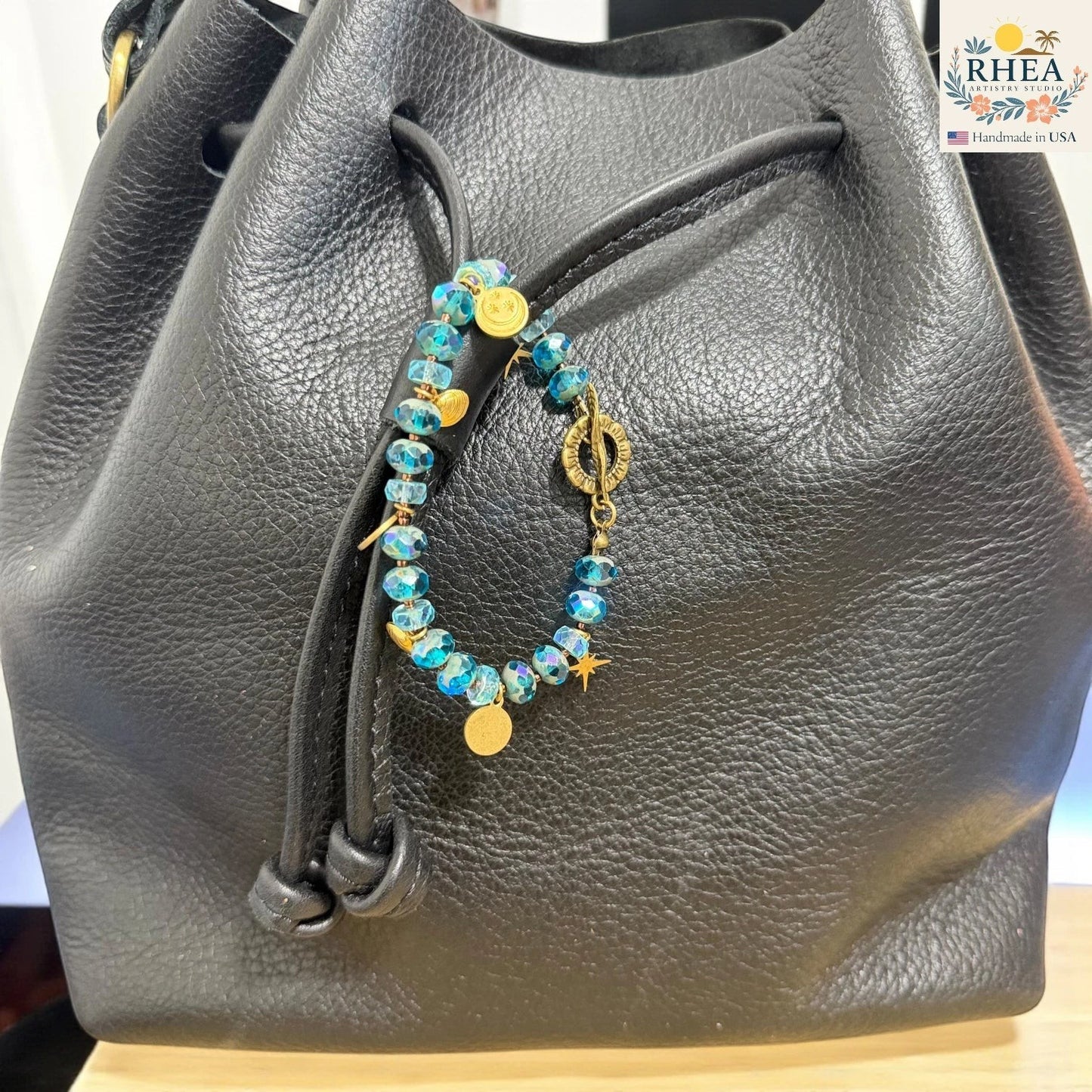 Black leather handbag with a beaded purse charm featuring ocean blue and gold beads.