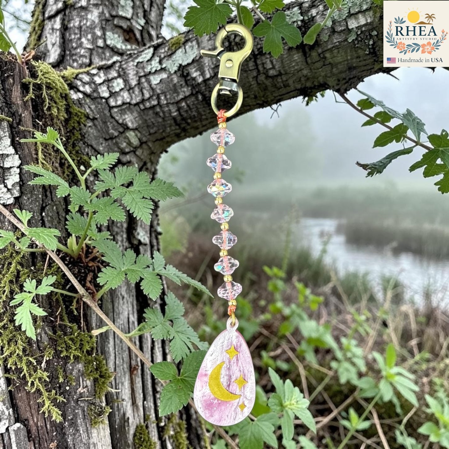 Decorative keychain with a moon and star design hanging from a tree branch with a natural background.