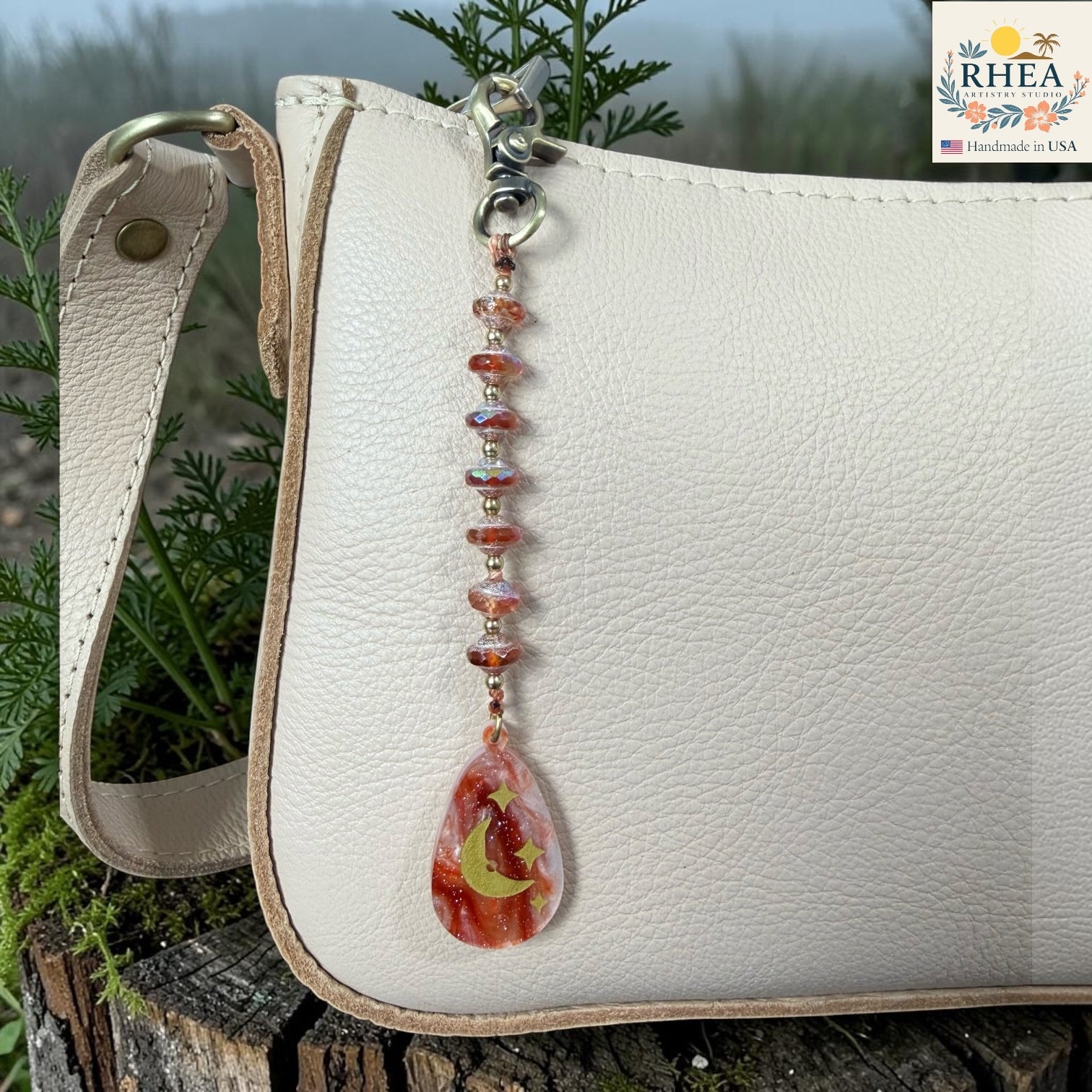 White leather bag with a decorative keychain featuring a teardrop-shaped pendant on a natural background.