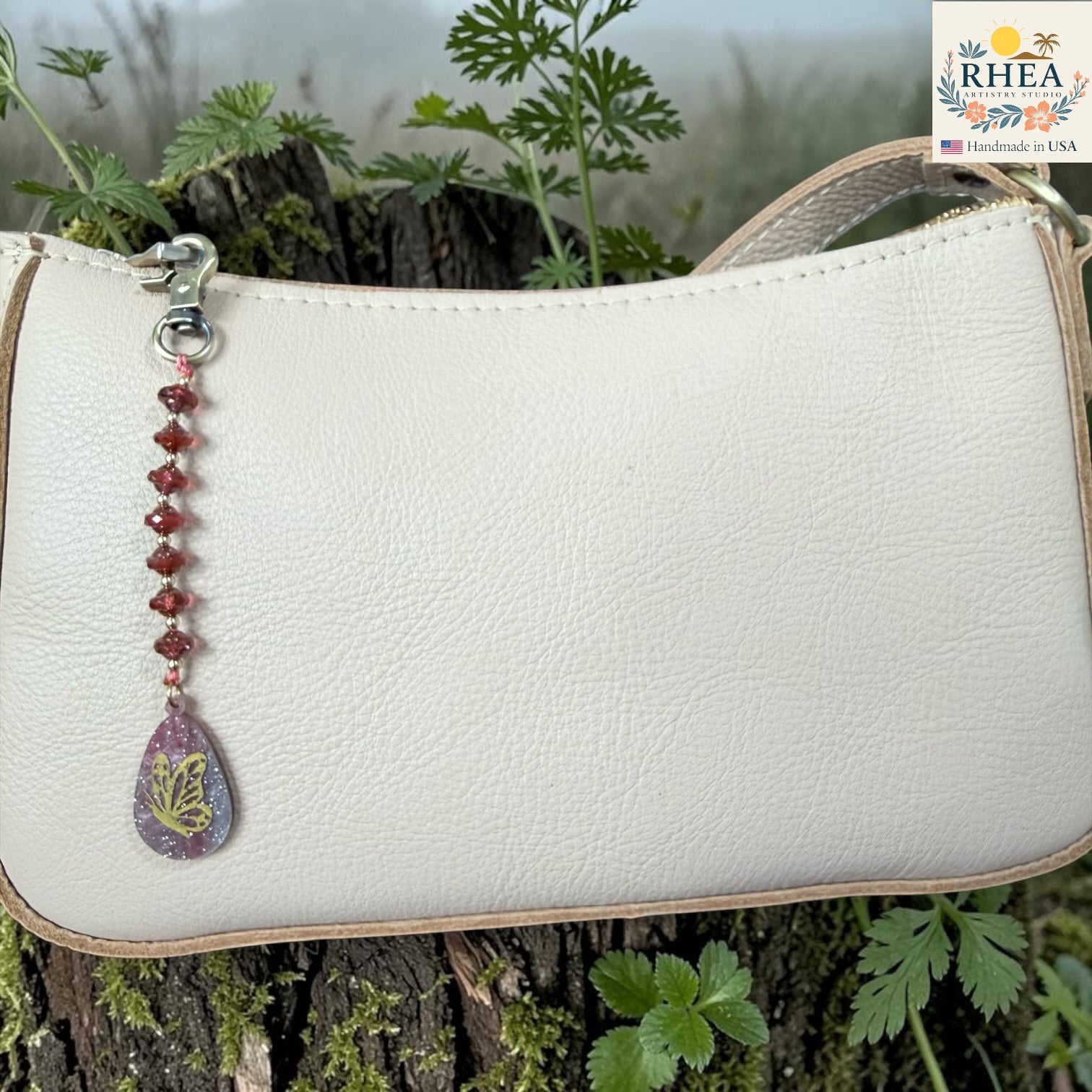 White handbag with a decorative keychain featuring a butterfly design, set against a natural background.