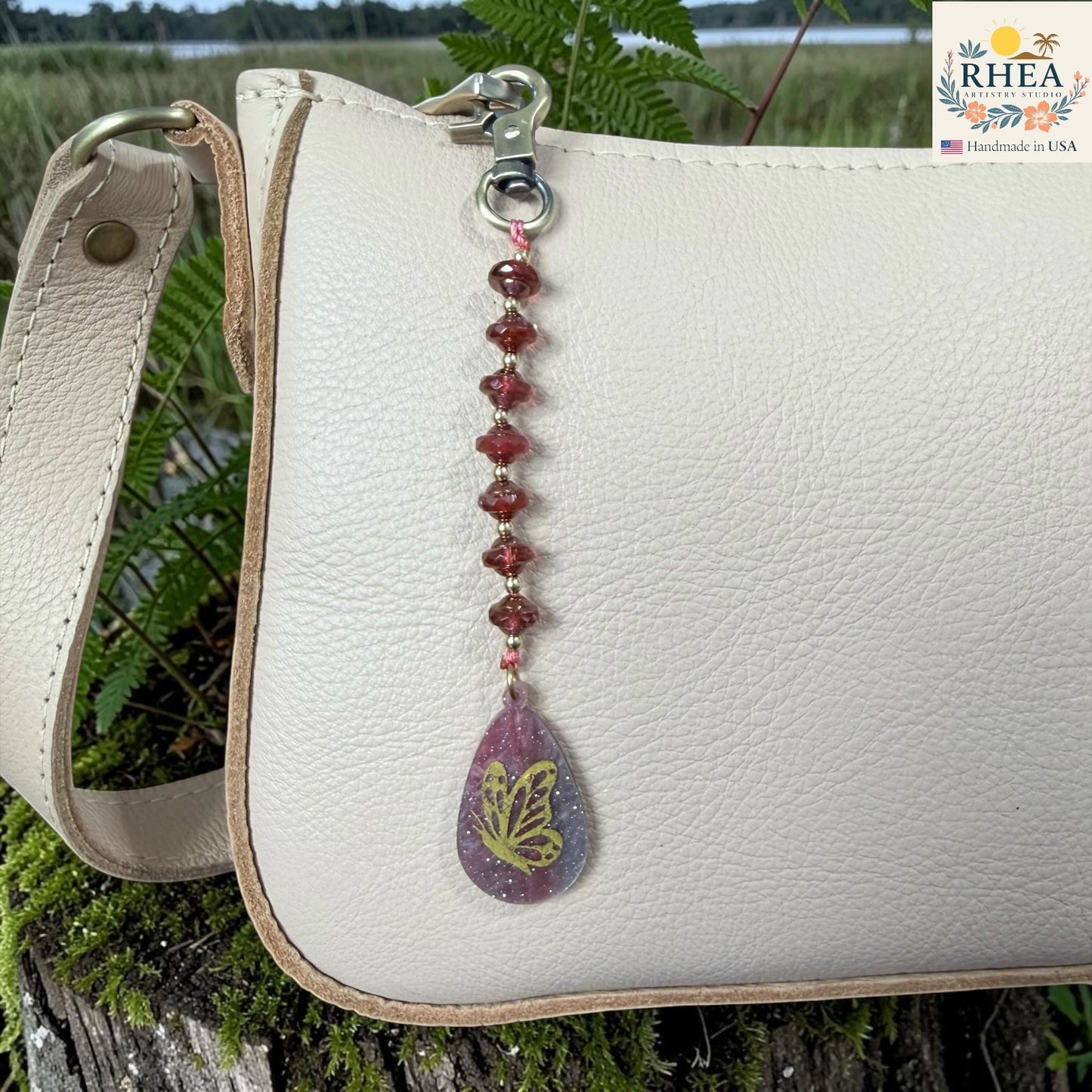 White leather bag with a decorative keychain featuring a butterfly design, set against a natural background.