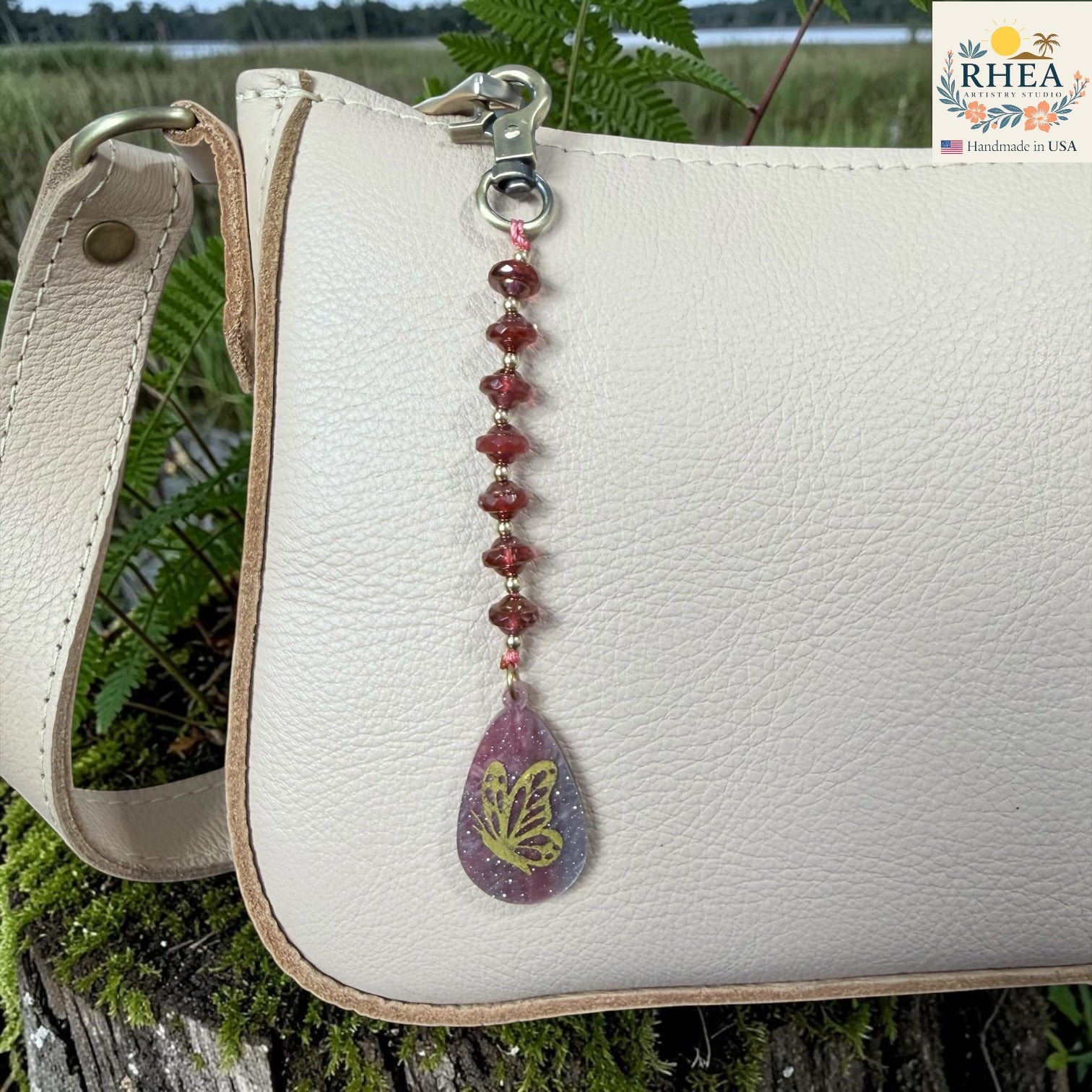 White leather bag with a decorative keychain featuring a butterfly design, set against a natural background.