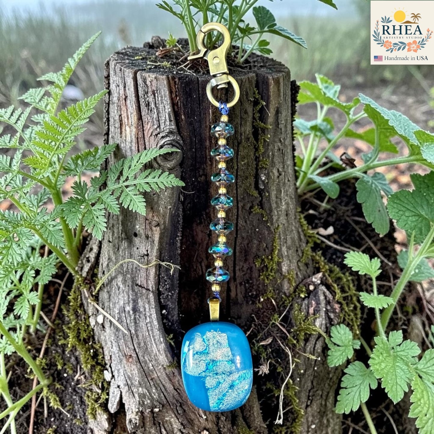 Keychain with blue stone and beaded chain on a wooden stump with plants