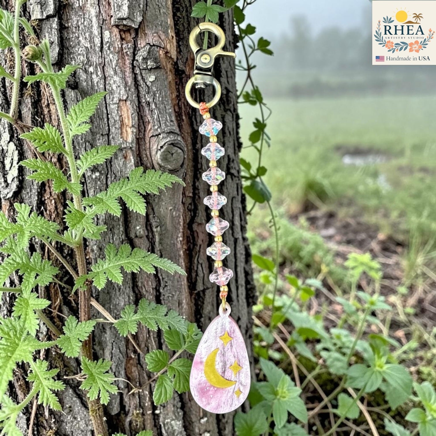 Decorative keychain with a teardrop pendant hanging on a tree branch with a natural background.