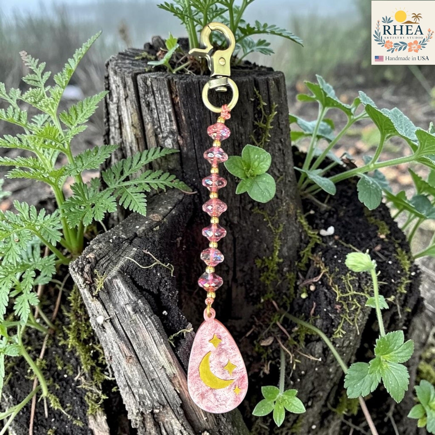 Pink keychain with moon and star design hanging from a plant
