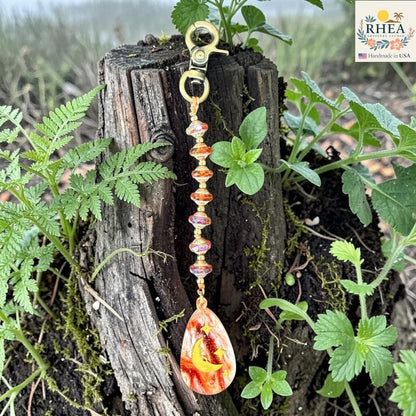 Decorative keychain with a colorful bead and orange teardrop charm on a wooden post with greenery.