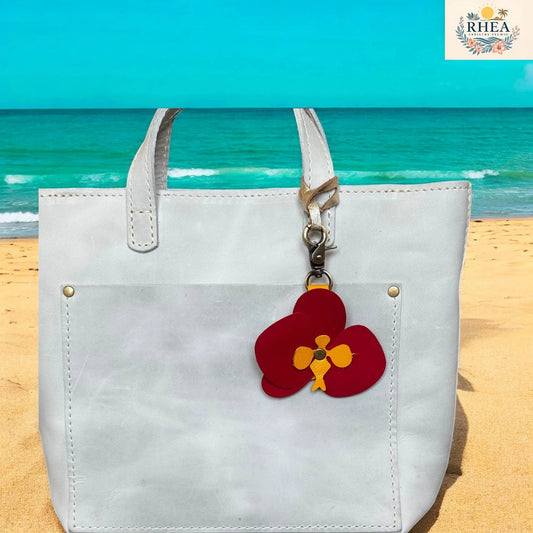 White tote bag with a red flower charm on a beach