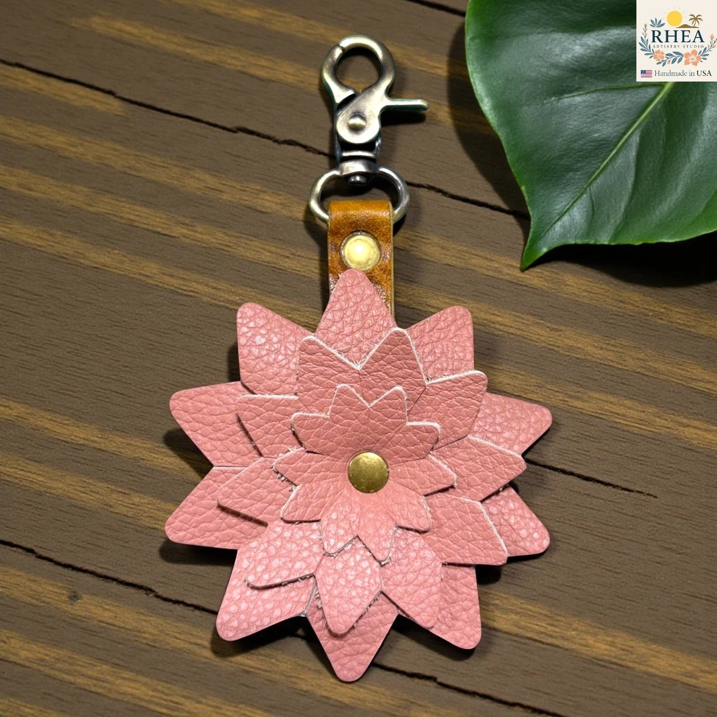 Pink flower-shaped keychain with a gold center on a wooden surface,  Statement leather flower charm for handbags and backpacks