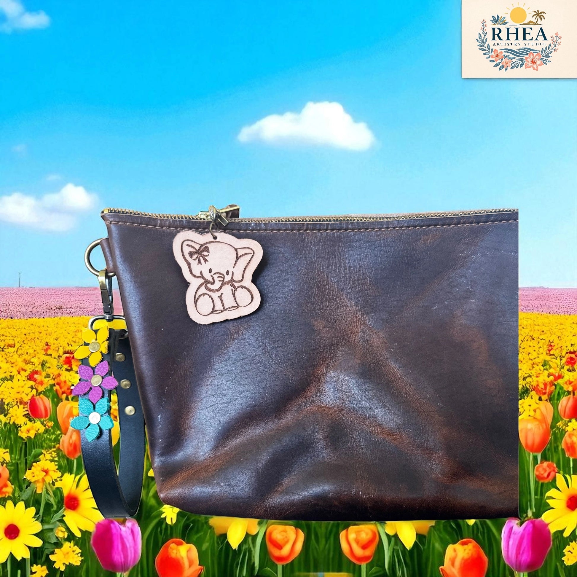 Brown leather pouch with a bear charm on a colorful floral background, featuring the RHEA brand.