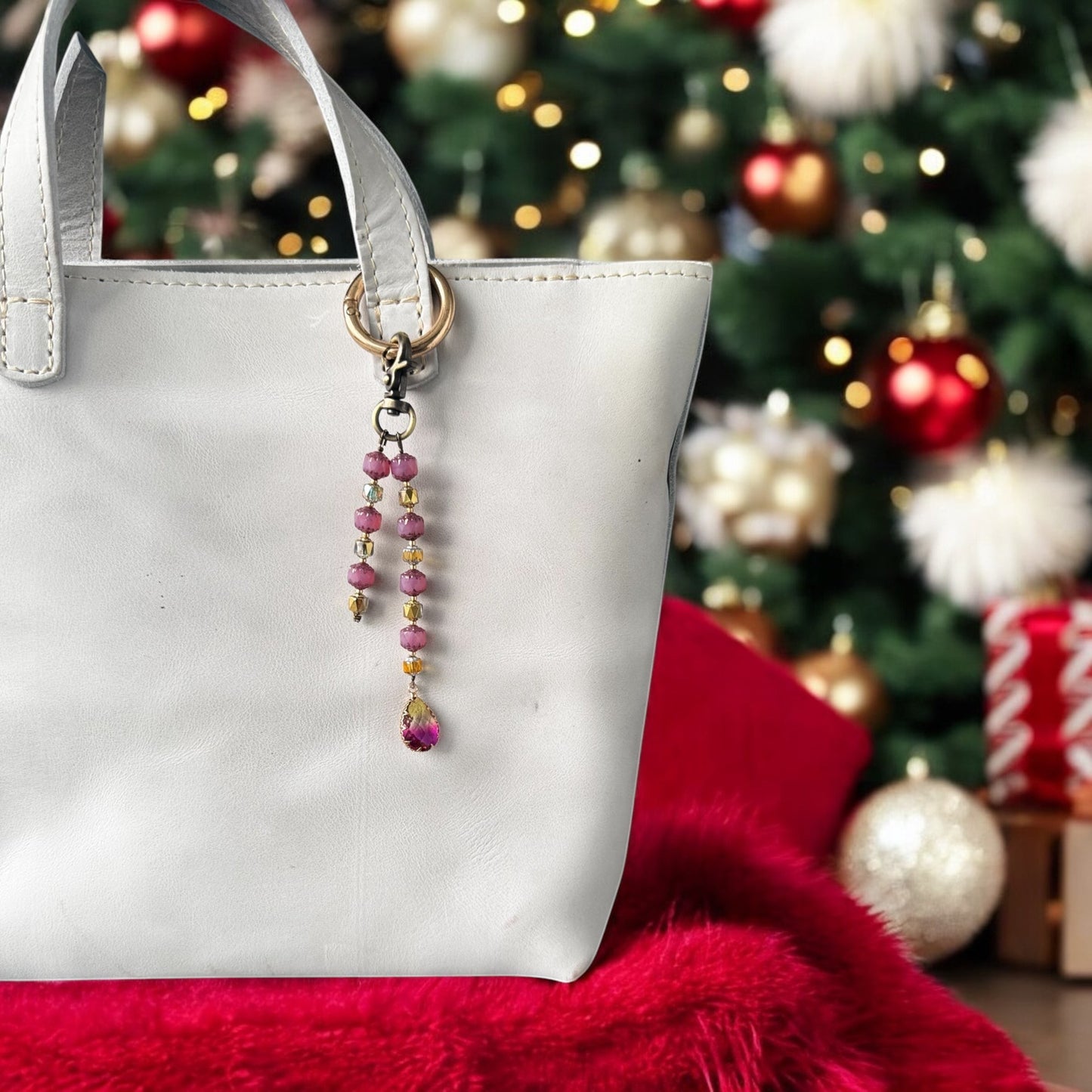 A white designer handbag with a crystal beaded keychain and a teardrop pendant, displayed against a festive background with Christmas decorations.