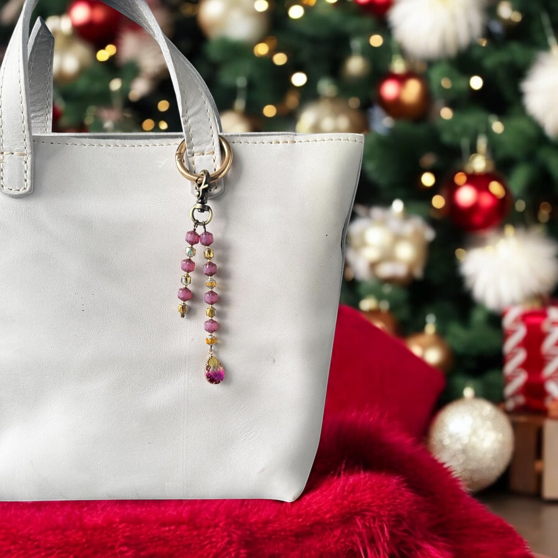 A white designer handbag with a crystal beaded keychain and a teardrop pendant, displayed against a festive background with Christmas decorations.