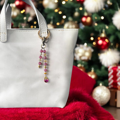 A white designer handbag with a crystal beaded keychain and a teardrop pendant, displayed against a festive background with Christmas decorations.