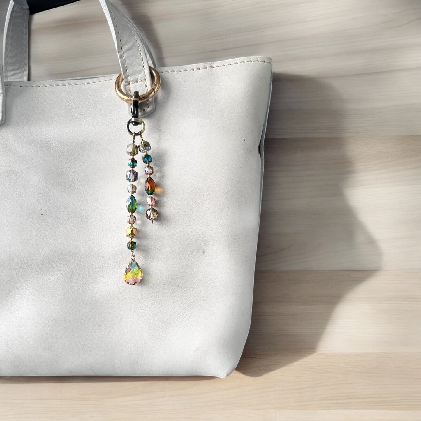 A white designer handbag with a crystal beaded keychain and a teardrop pendant, displayed against a festive background with Christmas decorations.