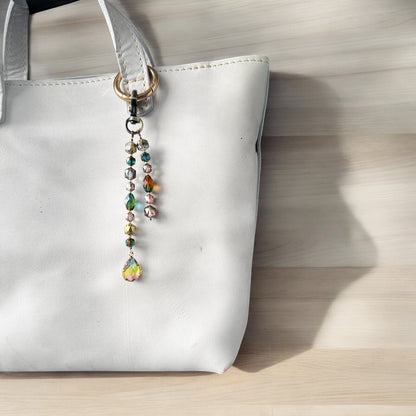 A white designer handbag with a crystal beaded keychain and a teardrop pendant, displayed against a festive background with Christmas decorations.