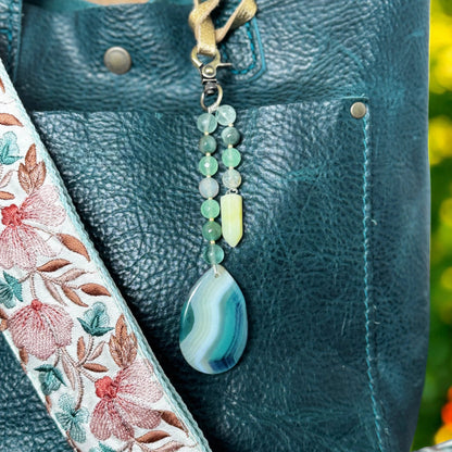 Decorative strap with floral embroidery and a teardrop pendant on a textured surface.