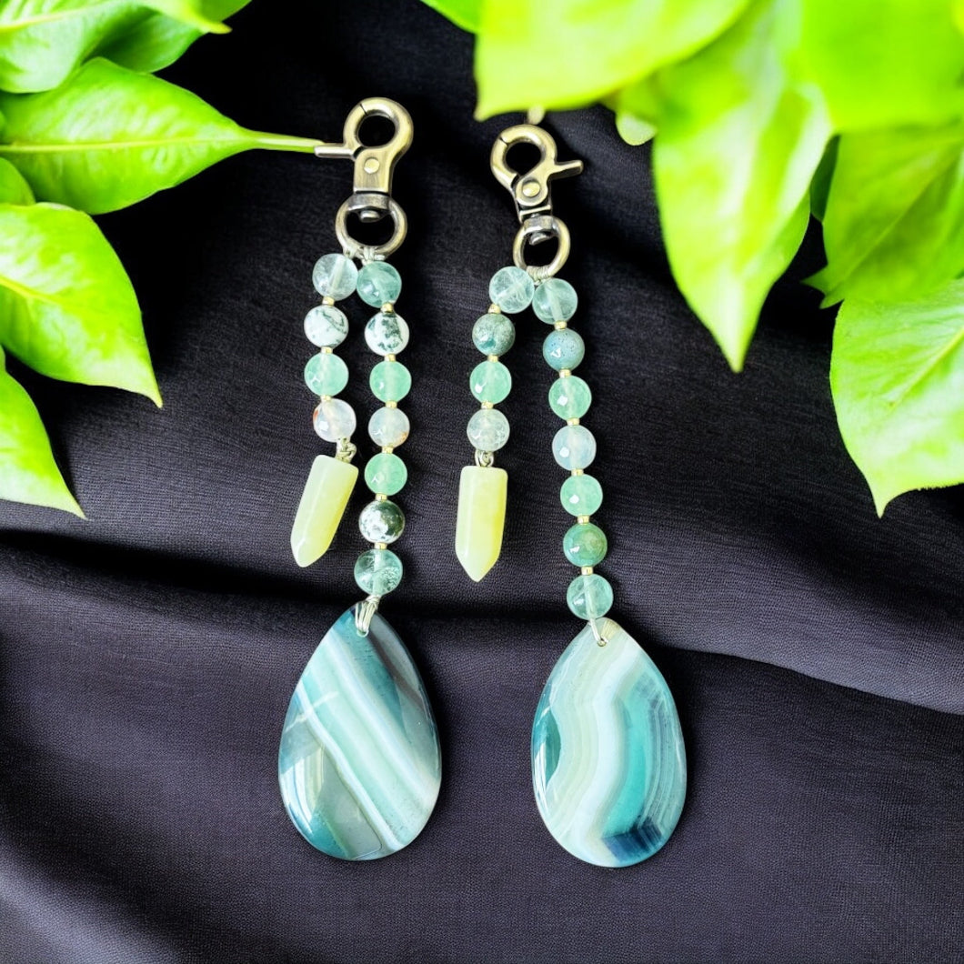 Pair of green beaded earrings with teardrop-shaped stones on a black fabric background with green leaves.