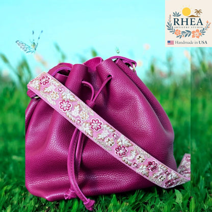 Pink leather bag with a floral strap on grass, RHEEA brand visible