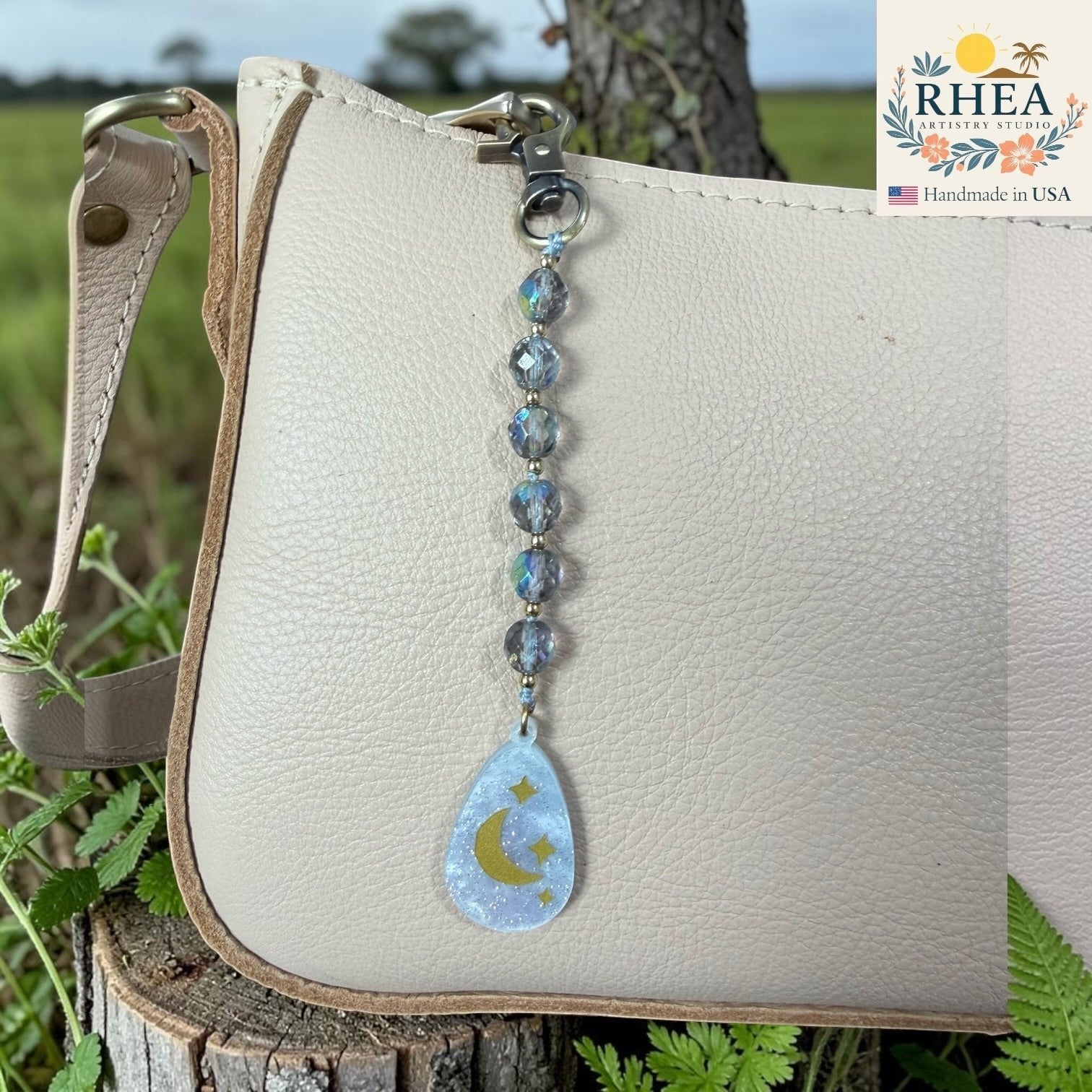 White handbag with a beaded keychain featuring a moon and star design, set against a natural background.