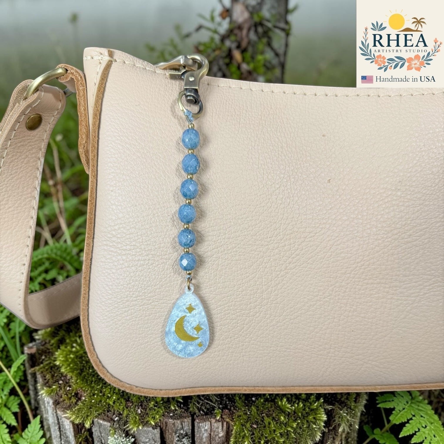 Beige handbag with a blue beaded keychain featuring a moon and star design, set against a natural background.