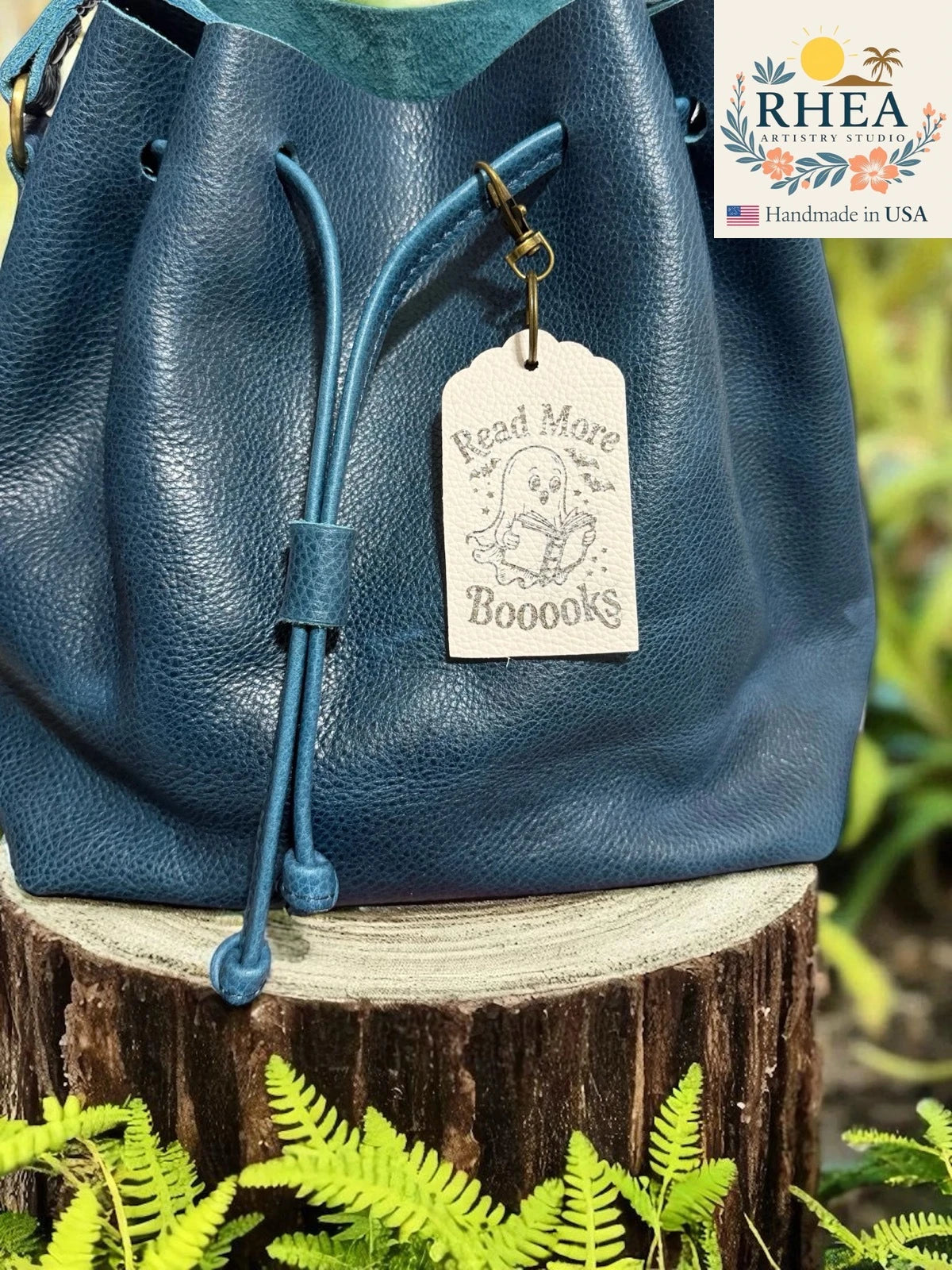 Blue leather bag with a leather tag on a wooden stump with greenery