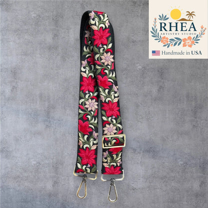 Floral embroidered purse strap with gold hardware on a gray background, featuring RHEA Artistry Studio logo.