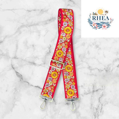 A floral embroidered purse strap in multicolor, attached to a black leather bag with brushed brass hardware.