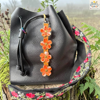 Rhea Artistry Studio Hand-Painted Leather Flower Bag Charm in Coral Honey with coral, orange, peach, and white painted leather flowers, brass rivets, honey leather strap, and antique brass clasp.