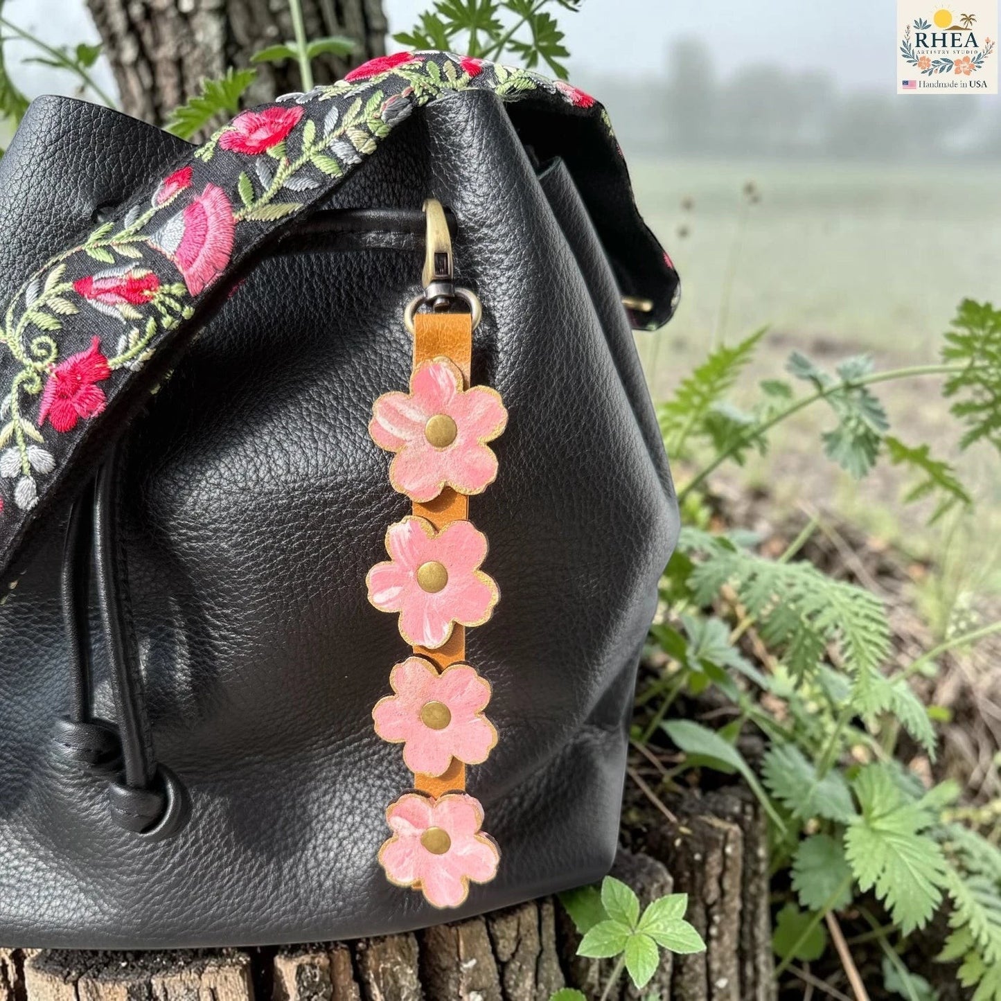 Rhea Artistry Studio Hand-Painted Leather Flower Bag Charm in Petal Cream with soft pale pink and cream painted leather flowers, brass rivets, honey leather strap, and antique brass clasp.