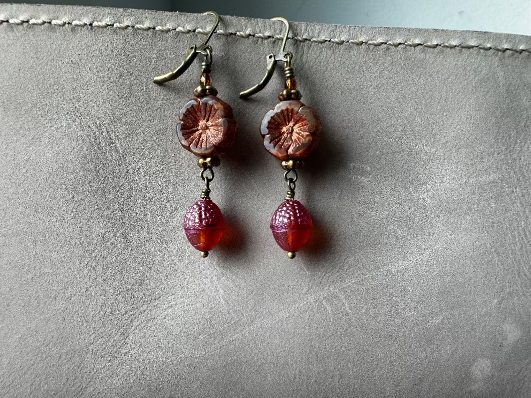 A pair of handcrafted Czech glass earrings with a serene glow, featuring a combination of rusty pink and brick orange hues, with brass hardware.