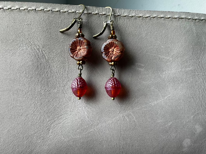 A pair of handcrafted Czech glass earrings with a serene glow, featuring a combination of rusty pink and brick orange hues, with brass hardware.