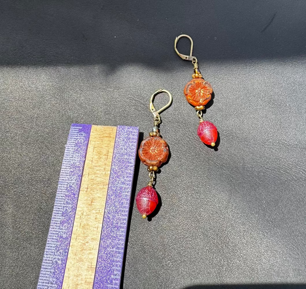 A pair of handcrafted Czech glass earrings with a serene glow, featuring a combination of rusty pink and brick orange hues, with brass hardware.