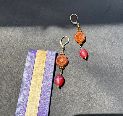 A pair of handcrafted Czech glass earrings with a serene glow, featuring a combination of rusty pink and brick orange hues, with brass hardware.