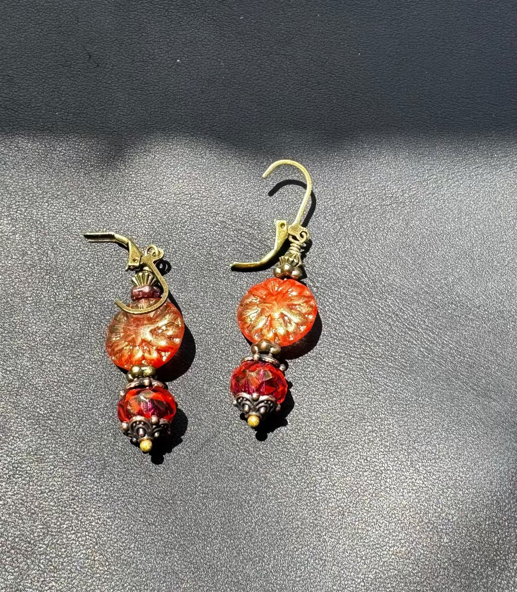 A pair of handcrafted Czech glass earrings with a serene glow, featuring a combination of rusty pink and brick orange hues, with brass hardware.