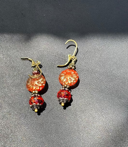 A pair of handcrafted Czech glass earrings with a serene glow, featuring a combination of rusty pink and brick orange hues, with brass hardware.
