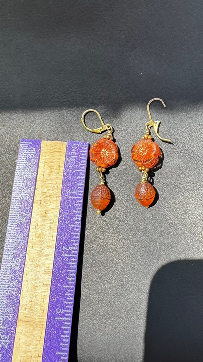 A pair of handcrafted Czech glass earrings with a serene glow, featuring a combination of rusty pink and brick orange hues, with brass hardware.