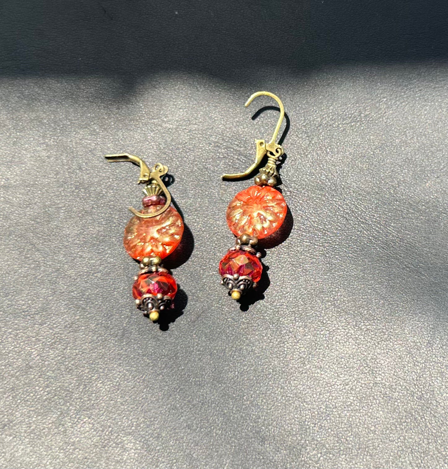 A pair of handcrafted Czech glass earrings with a serene glow, featuring a combination of rusty pink and brick orange hues, with brass hardware.