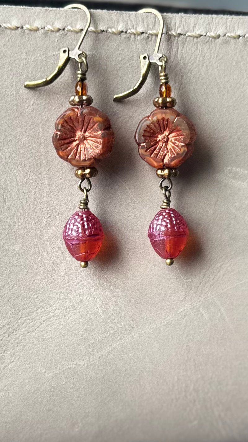 A pair of handcrafted Czech glass earrings with a serene glow, featuring a combination of rusty pink and brick orange hues, with brass hardware.