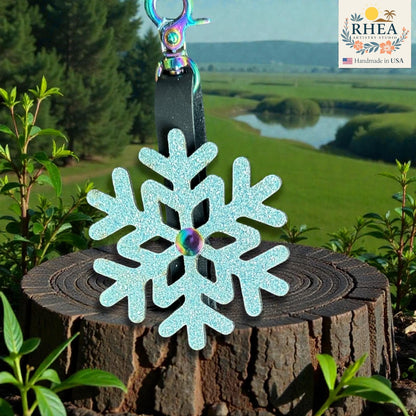 Decorative snowflake charm on a wooden stump with a scenic background and RHEA branding.