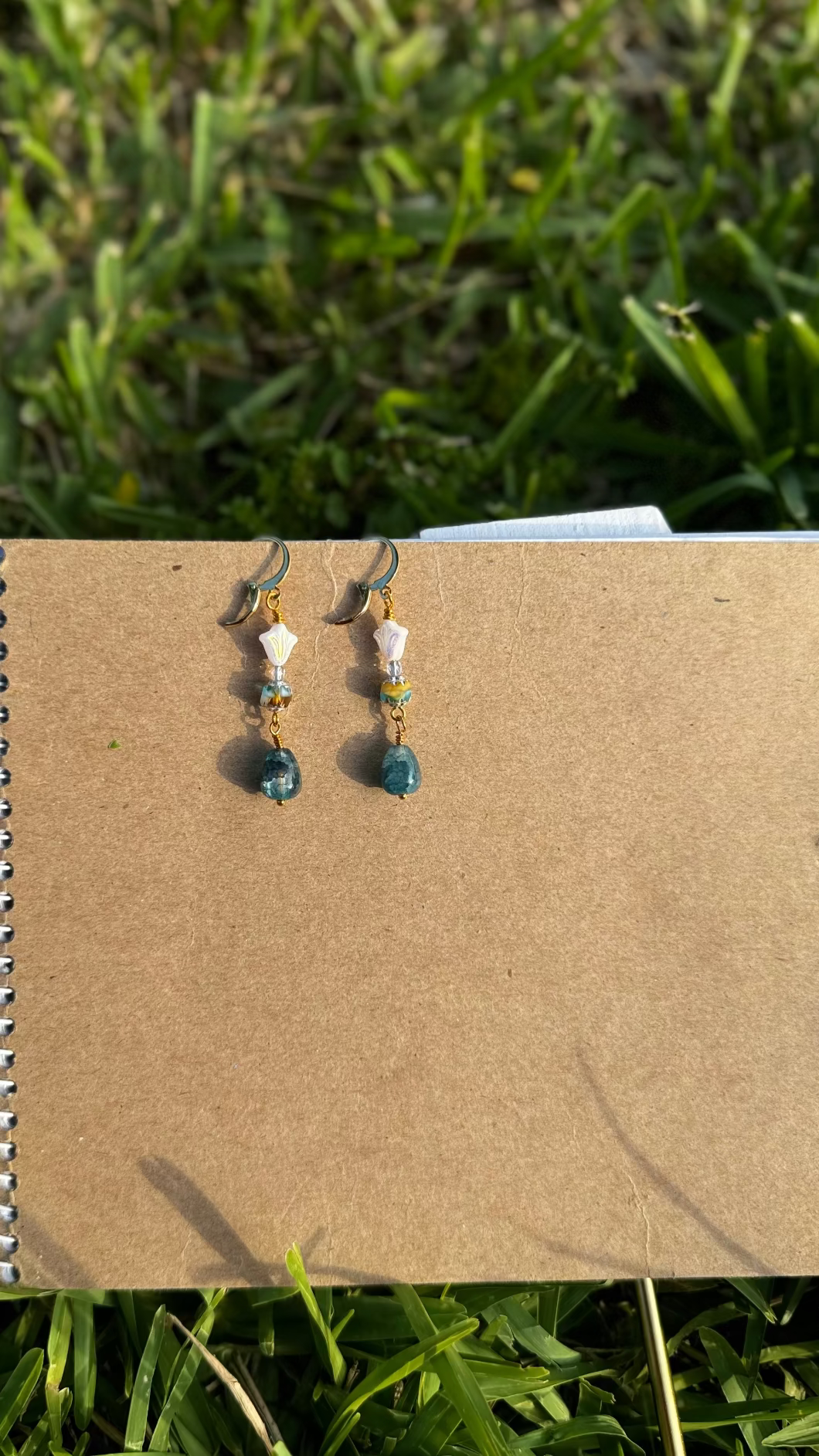A pair of gold-colored three petal cathedral drop earrings with white and blue czech glass accents, displayed against a beige background.