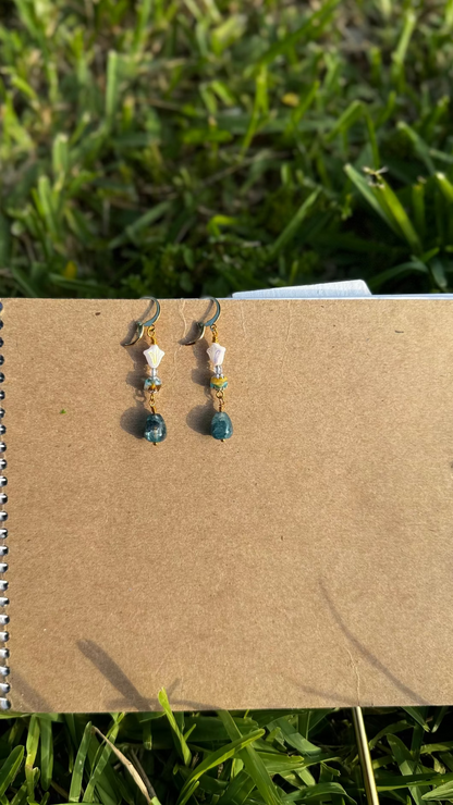 A pair of gold-colored three petal cathedral drop earrings with white and blue czech glass accents, displayed against a beige background.