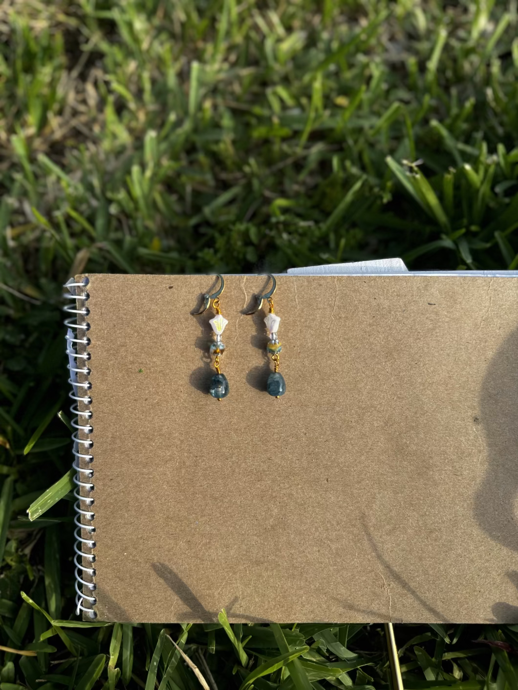 A pair of gold-colored three petal cathedral drop earrings with white and blue czech glass accents, displayed against a beige background.