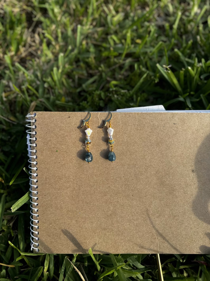 A pair of gold-colored three petal cathedral drop earrings with white and blue czech glass accents, displayed against a beige background.