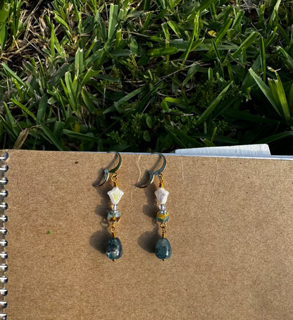 A pair of gold-colored three petal cathedral drop earrings with white and blue czech glass accents, displayed against a beige background.