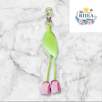 Green and purple keychain on a white surface with grass and flowers in the background