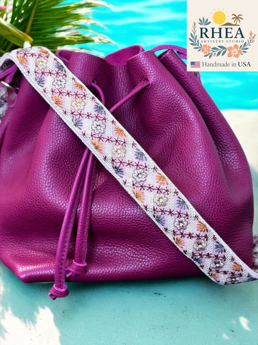Purple leather bag with a floral strap on a turquoise surface, RHEA brand visible.