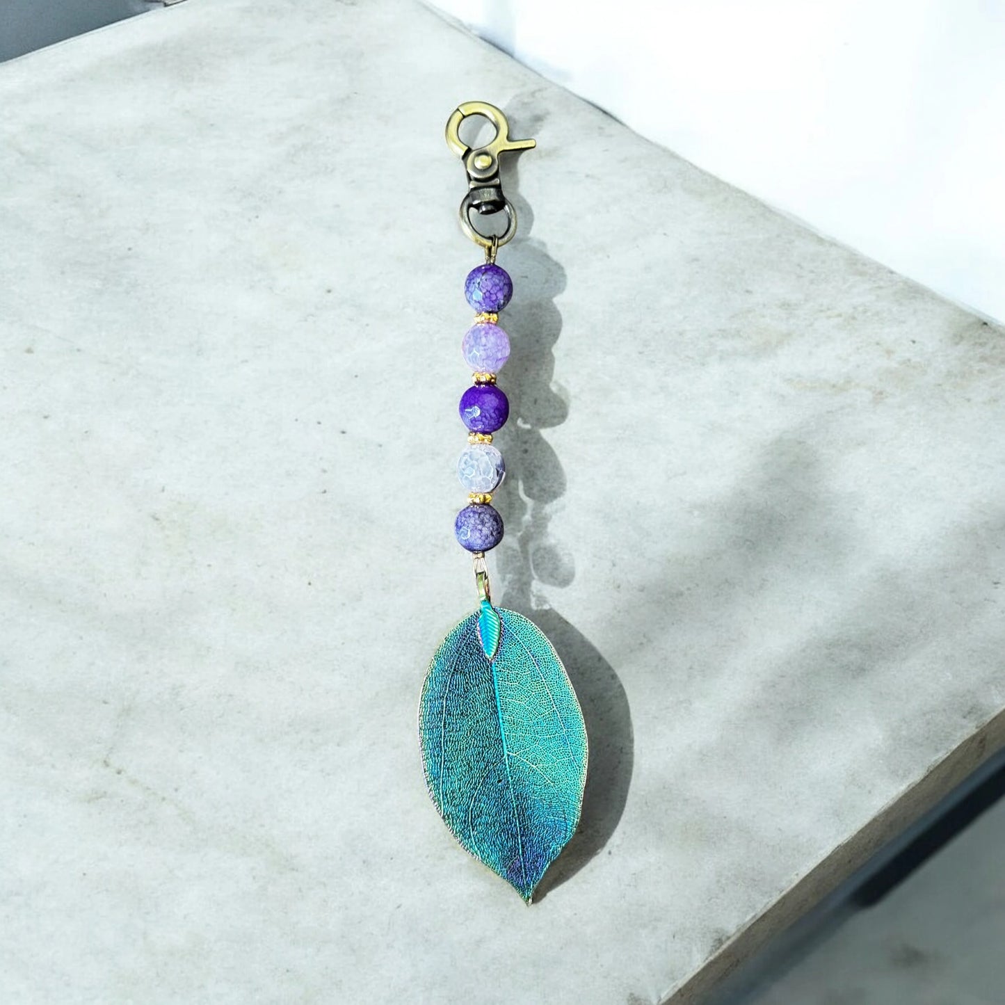 Keychain with teal leaf pendant and purple beads on a marble surface