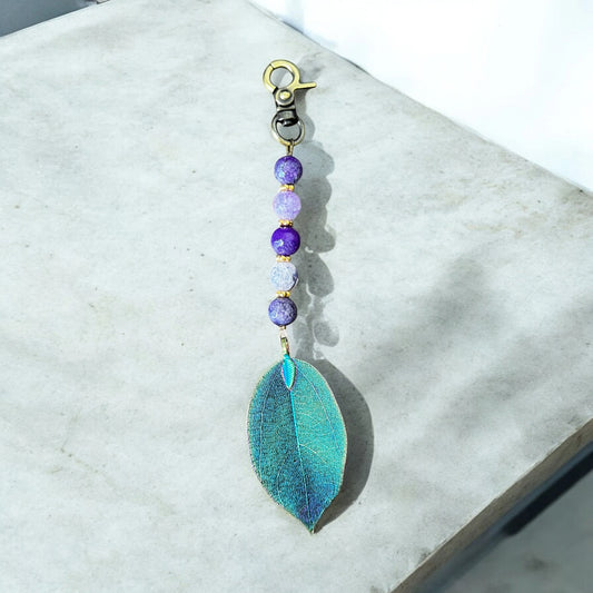 Keychain with teal leaf pendant and purple beads on a marble surface