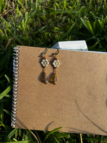 A pair of white hibiscus gold drop earrings with gold plated brass findings, displayed on a notebook.
