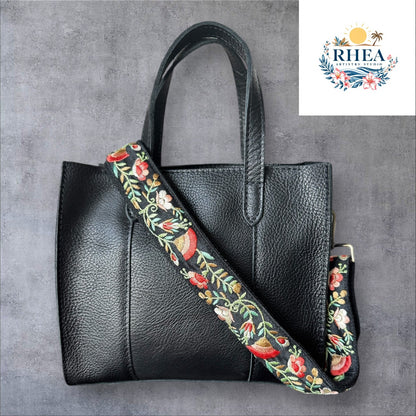 An adjustable embroidered purse strap with a floral pattern and gold hardware, displayed against a grey background.