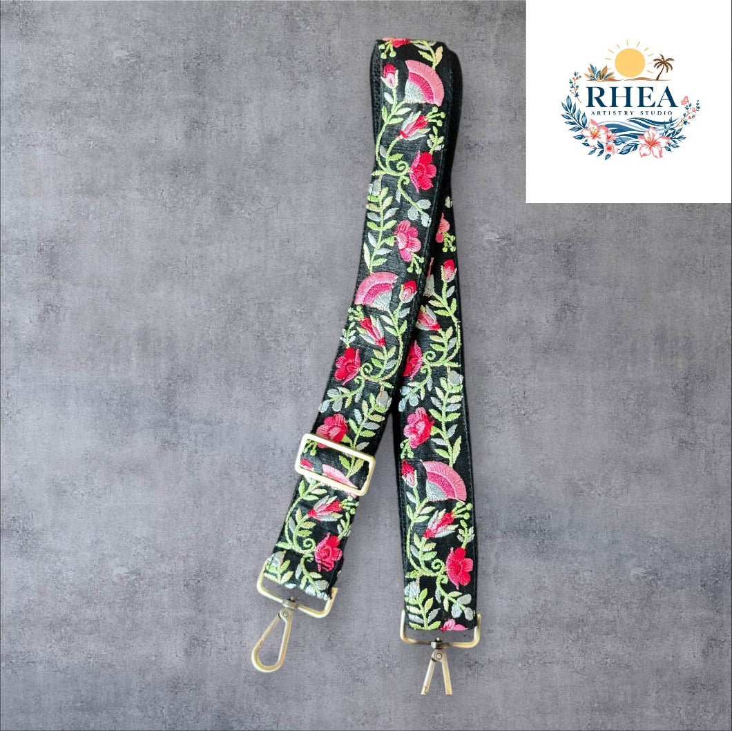 An adjustable embroidered purse strap with a floral pattern and gold hardware, displayed against a grey background.
